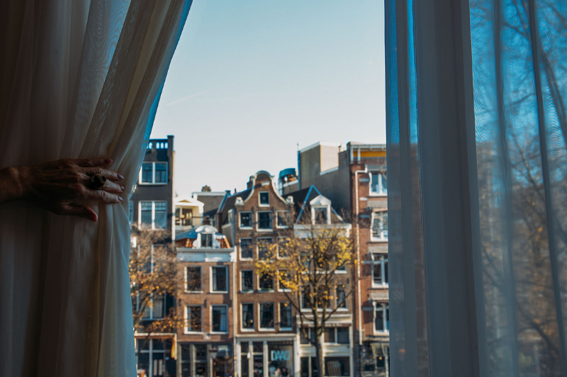 Guest opening the curtains in a room at the ambassade hotel in amsterdam, revealing a view of historic canal houses.