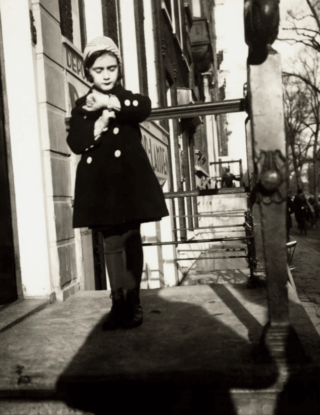 Historic photo of anne frank standing on the stairs of a canal house in amsterdam.