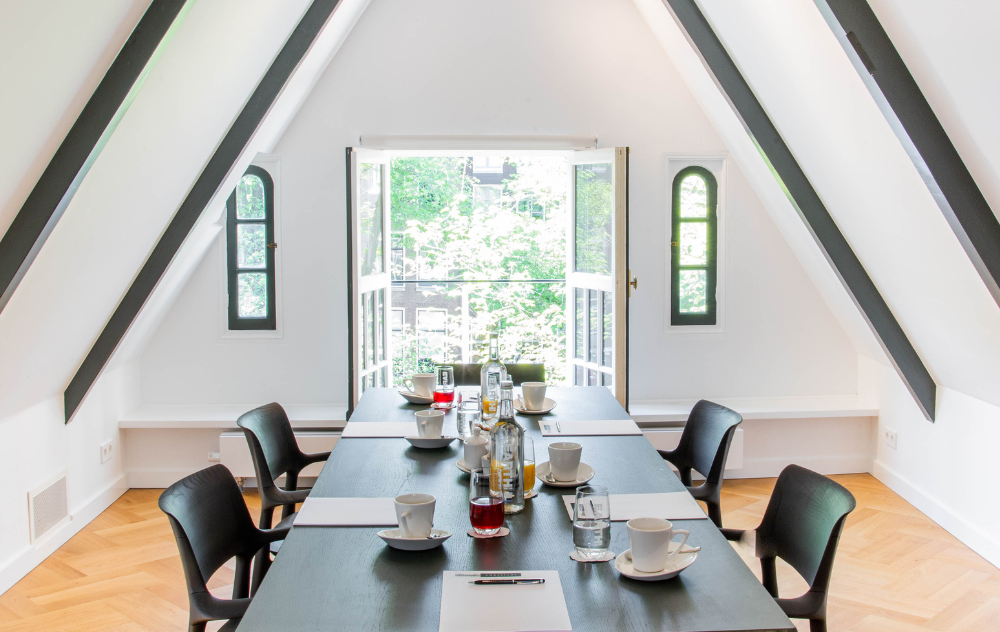 Bright meeting space in the attic at the ambassade hotel with open doors and natural daylight.