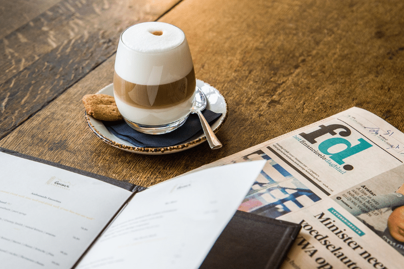 Cup of coffee with a newspaper and menu on the table.