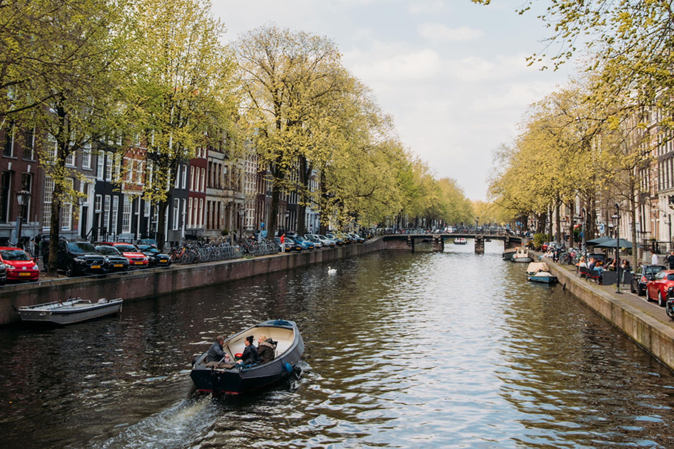 Historic canal houses along the herengracht with a boat passing by.